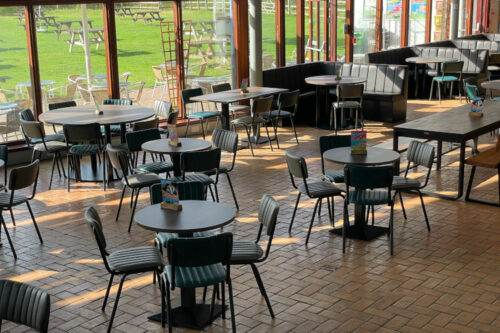 Various tables, bench seating and chairs in a large cafe space.