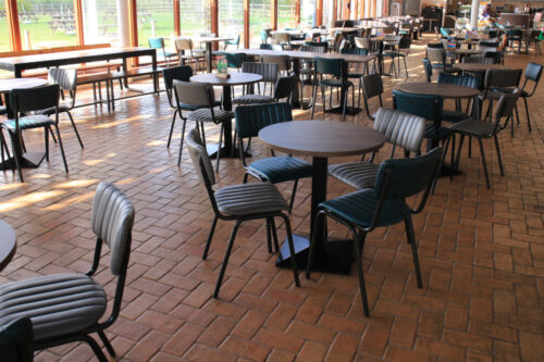 Large group of dining tables and dining chairs in a community centre style space.