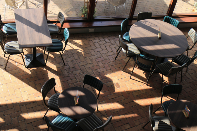 Round and rectangle dining tables with chairs from a birds eye view near large windows.