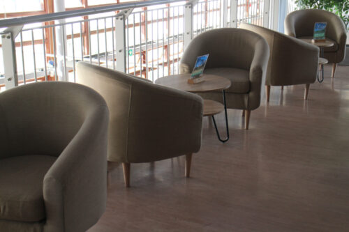Natural coloured tub chairs on a balcony, with small coffee tables.