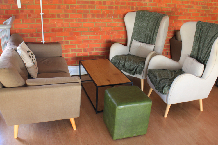 Large winged armchairs, sofa and coffee table against a brick wall in a coffee shop.