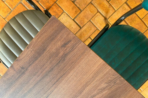 birds eye view angle of walnut dining table top with two dining chairs, one in teal, one in grey.