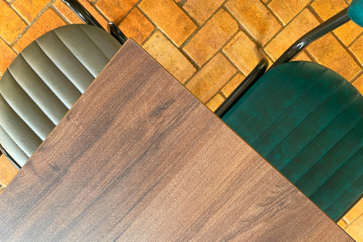 birds eye view angle of walnut dining table top with two dining chairs, one in teal, one in grey.