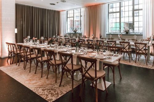 Cross back dining chairs with white dining tables, at a wedding in a hotel event space.