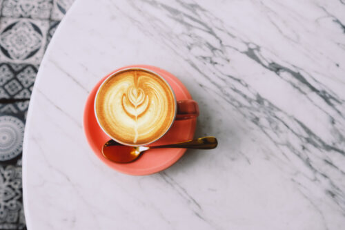 Trendy pink cup of hot cappuccino on marble table background. beautiful latte art on the top.