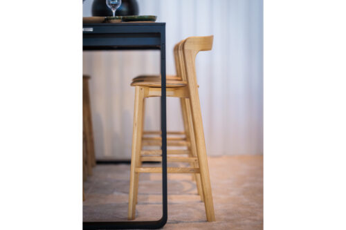 Nina bar stool in natural oak, side view, paired with a black flow poseur table, from Flexfurn.