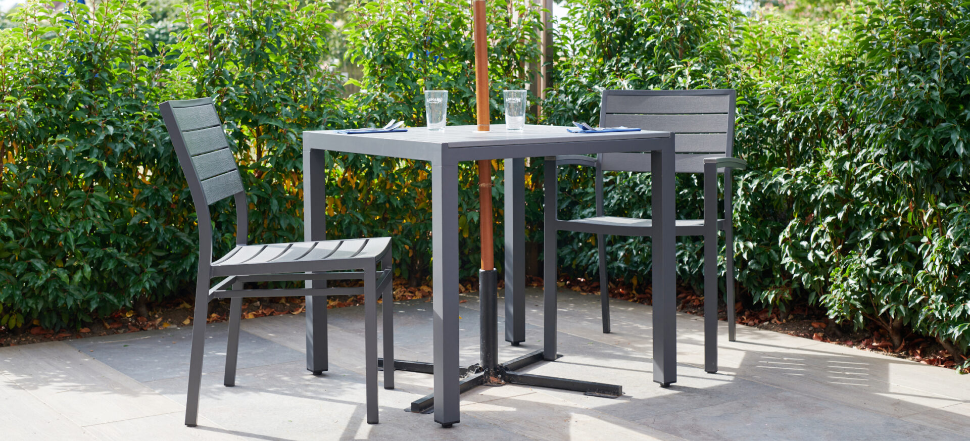 Venue side chair, armchair and square dining table, grey metal frame with grey wood effect slats, in a pub garden.