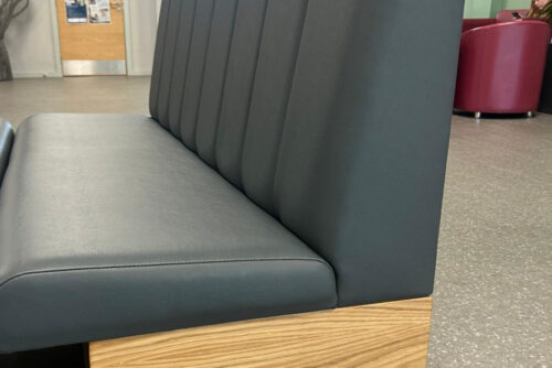 Cosmopolitan bench seating with a fluted backrest, grey faux leather and oak veneer, in a school.