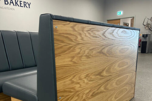 Cosmopolitan bench seating with a fluted backrest, grey faux leather and oak veneer, in a school.