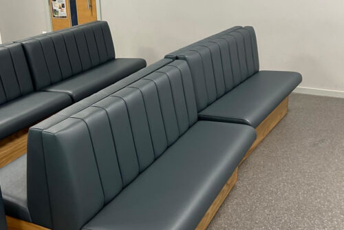 Cosmopolitan bench seating with a fluted backrest, grey faux leather and oak veneer, in a school.