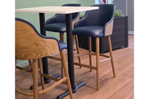 Zeni bar stools in blue faux leather, oak veneer backrest and a rectangle poseur table in white, in a school breakout area.