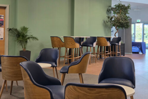 Dining and poseur tables with Dining chairs and bar stools in a blue faux leather, and wooden back. Located in a dining room.
